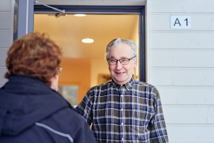 Valokuvassa kaksi ihmistä kohtaamassa toisensa ulko-ovella.