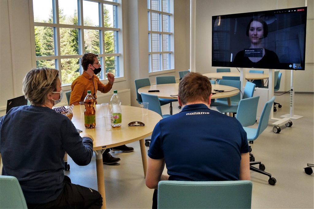 Valokuvassa kolme ihmistä luokkatilassa katseet suunnattuna tv-ruudulle.