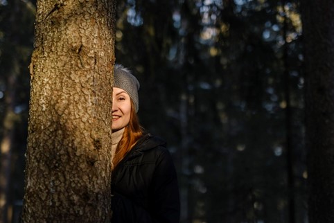 Valokuva, jossa ihminen kurkistaa puunrungon takaa.