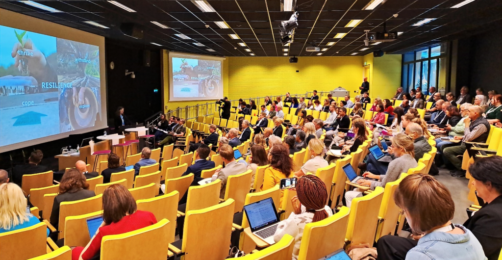 A photograph of many people sitting in a large lecture hall.